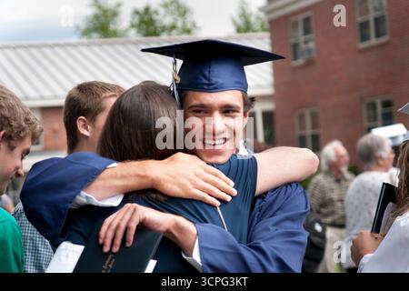 A young graduate smiles and hugs his mother after having received his high school diploma. Stock Photo