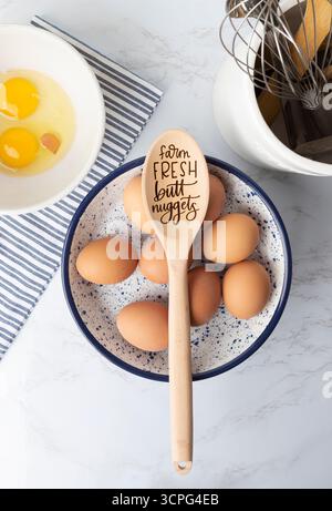 Whole and cracked eggs in bowls on marble countertop with utensils Stock Photo