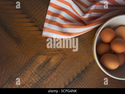Wood tabletop with bowl of brown eggs and dishtowel in rustic kitchen Stock Photo