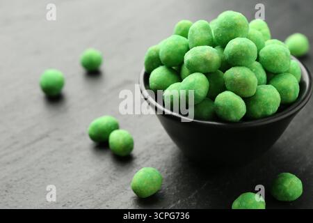 Delicious wasabi coated peanuts and bowl on dark textured table, closeup Stock Photo
