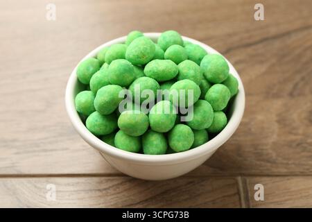 Delicious wasabi coated peanuts in bowl on wooden table, closeup Stock Photo