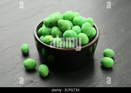 Delicious wasabi coated peanuts and bowl on dark textured table, closeup Stock Photo