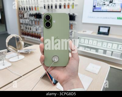 Poznan, Poland - September 20, 2025: A hand holds iPhone 17 green phone, showing Apple logo, dual camera, anti-theft cable in electronics store Stock Photo