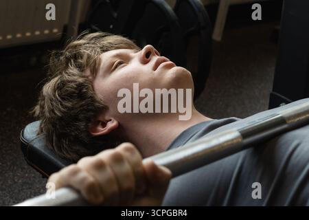 Young caucasian and sporty man doing bench press exercise with barbell in modern gym. Chest workout. Close up. Stock Photo
