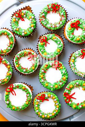 Festive cupcakes decorated with colorful wreath designs, featuring red bows and green decorative elements on a gray platter Stock Photo