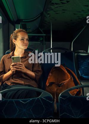 Female passenger sitting in public transport with phone evening ride Stock Photo