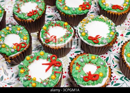Festive cupcakes decorated with colorful wreath designs, featuring red bows and green decorative elements on a gray platter Stock Photo