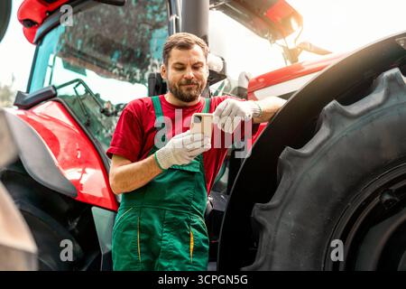 Man agricultural worker using his smartphone near the tractor outdoors. Stock Photo