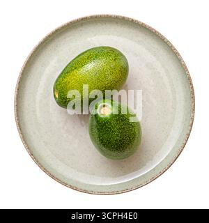 Two ripe avocados on a green plate. Top view of two fresh avocados on a ceramic plate, isolated on a white background. Stock Photo