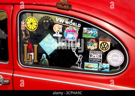 close up detailVintage red volkswagen beetle car with a rear window full of colorful stickers showcasing various logos, icons, and travel destinations Stock Photo