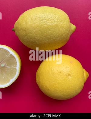 Fresh lemon pattern on a vivid pink background. Flat lay. Lemons. Vitamin C. Creative minimal art. Minimal summer concept. Whole and halved lemon. Stock Photo
