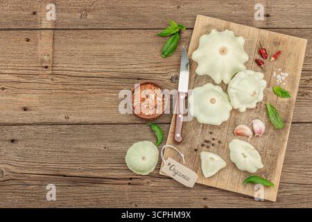 Pattypan squash on a wooden cutting board with a knife, garlic, fresh basil, and various spices. Clean eating concept with fresh organic ingredients r Stock Photo