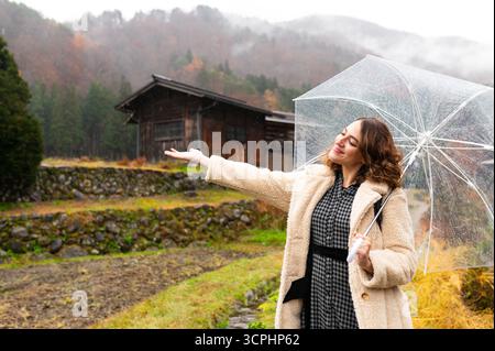 Smiling Woman Enjoying Rain with Transparent Umbrella in Japanese Countryside Stock Photo