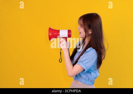 woman shouting through megaphone against bold yellow background, expressing energy and announcement Stock Photo