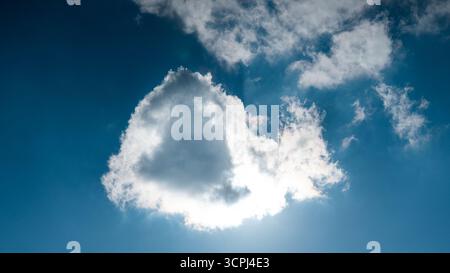 Bright sun shining behind white cloud in blue sky with atmospheric light and shadow. Stock Photo