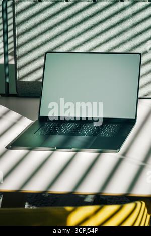 Laptop screen mockup office desk sunlight shadows. Minimalistic scene with modern laptop featuring blank screen placed on white desk with creative sun Stock Photo