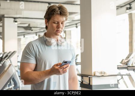 Athlete man with mobile phone standing at gym. Warming up. Preparation for cardio training. Trainer waiting for client. Close up. Stock Photo