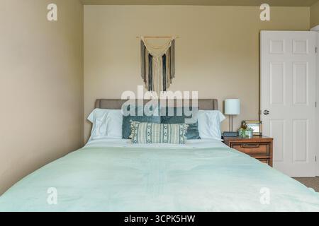 Bedroom blue green pillows, bed, headboard, macrame wall art, nightstand, lamp, front view desert southwest theme Stock Photo