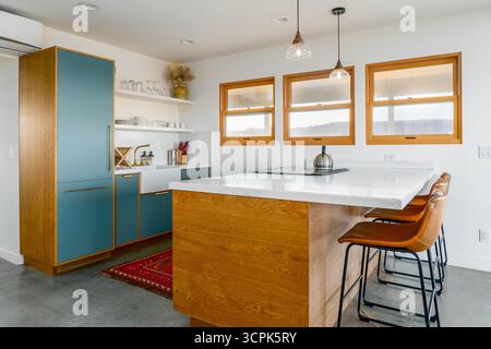 Minimal modern kitchen with turquoise cabinets windows leather breakfast bar stools concrete floor in desert home Stock Photo