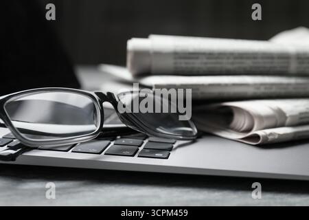 Stack of newspapers, laptop and glasses on grey table, closeup Stock Photo