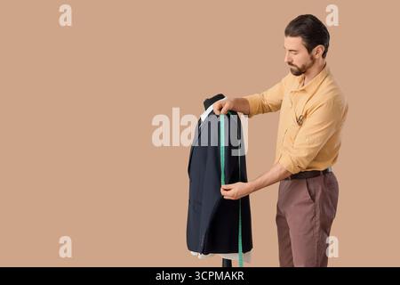 Male tailor measuring jacket on beige background Stock Photo