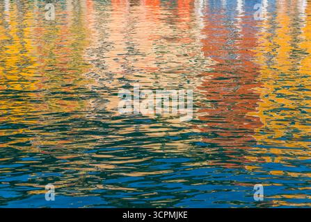 Colorful reflections of buildings dance on the surface of Portofino Harbor's water. Hues of yellow, orange, blue, and red create a vivid mosaic. Stock Photo