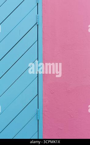 Blue door with diagonal timber panels next to a smooth, pink rendered wall. The hinges are also painted blue, matching the door. Stock Photo
