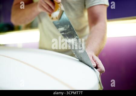 Hands, person and cutting surfboard in workshop for custom design, shaping guide and repair work. Worker, carving equipment and board for crafting Stock Photo