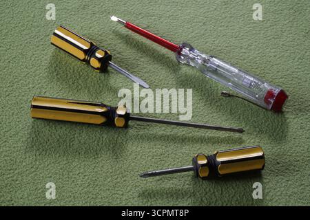 Yellow phillips screwdriver, tri-wing screwdriver and white red test pen on green background. Electrical repair equipment. Stock Photo