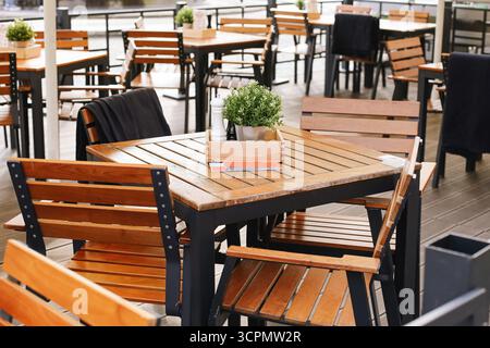 Outdoor cafe terrace with wooden tables and chairs. Empty restaurant furniture arranged outside. Dining area for guests in open air. Stock Photo