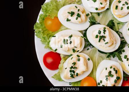 Stuffed deviled eggs with chives on lettuce leaves. Fresh appetizer served on plate. Healthy homemade meal with egg and vegetable decoration. Stock Photo