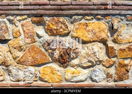 A striking wall constructed of natural stones, showcasing an array of warm colors and unique textures under bright sunlight. Perfect for rustic or vin Stock Photo