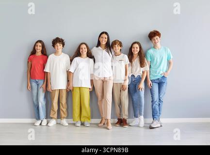 Portrait Of Happy Teacher And Group Of Students Standing On Grey Background Stock Photo