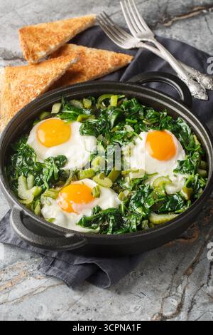 Green shakshuka is a stew of eggs in a mixture of greens, herbs and other vegetables such as spinach, celery, peppers and green onions close-up in a f Stock Photo