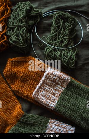Cozy knitted socks with yarn ball and knitting needles. Striped wool socks on dark green sheet. Cozy autumn colours. Woven crochet close up. Stock Photo