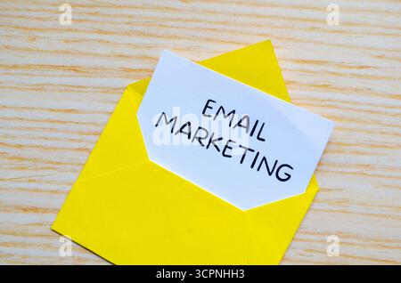 Email marketing text written on yellow notepad with envelope illustration clipped on wooden desk Stock Photo