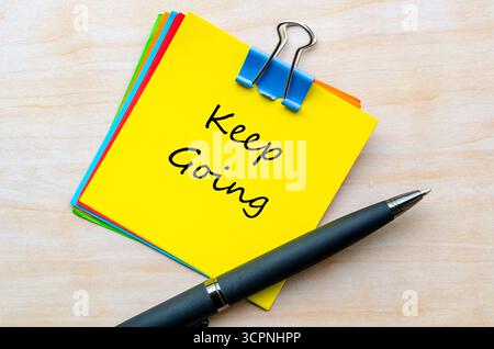 Keep going motivational handwritten text on yellow notepad clipped on wooden desk Stock Photo