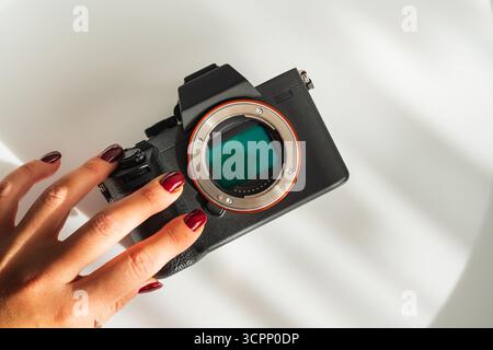 Female photographer holds a modern mirrorless digital camera, showing the open matrix sensor for maintenance or cleaning. Stock Photo