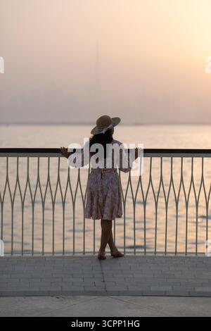 young tourist woman walking on waterfront promenade at Dubai creek harbor with Dubai downtown skyline in background Stock Photo