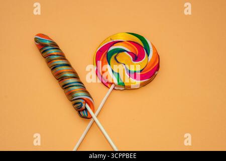 Colorful lollipops on vibrant orange background. A bright and cheerful image featuring two colorful lollipops placed on an orange backdrop. Stock Photo