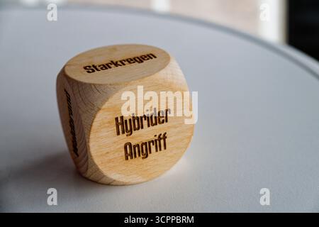 A smooth wooden cube bears the phrase hybrider angriff on the front face suggesting a theme of hybrid attack and modern risk while the rounded shape o Stock Photo