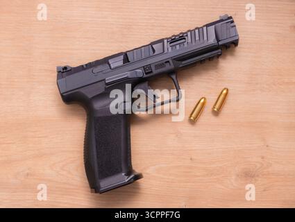 A modern semi-automatic pistol top view on a wooden surface next to two golden bullets. The sleek design and metallic finish highlight its advanced. Stock Photo