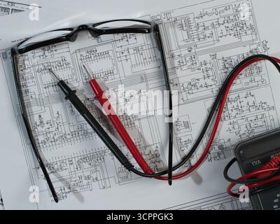 Electronic Schematic Multimeter and Glasses - Overhead view of a multimeter's probes and reading glasses resting on complex electronic circuit diagram Stock Photo