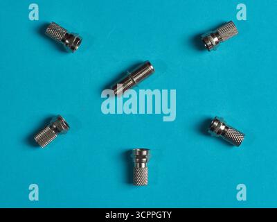 F-Type Coaxial Connectors Blue Backdrop - Three shiny metal F-type coaxial cable connectors scattered on a bright turquoise blue background. Focus on Stock Photo