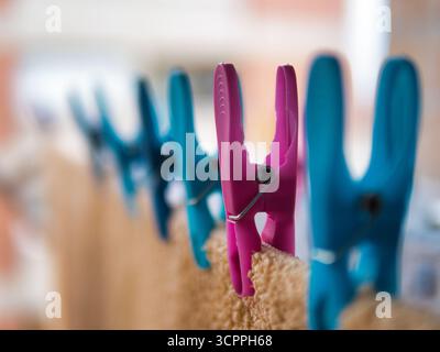 Pink Clothespin Focus Blue Line Blur - Bright pink and blue plastic clothespins gripping a towel on a clothesline. Shallow depth of field for a fresh Stock Photo