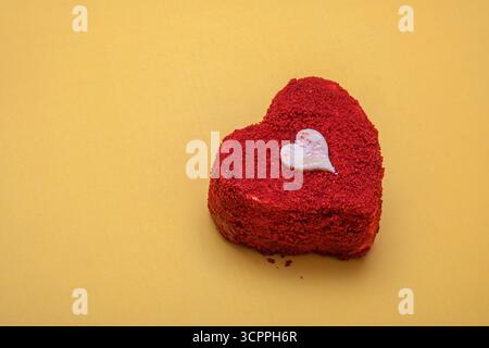 Heart-Shaped red velvet cake on yellow background. Valentine’s Day, anniversaries, or special celebrations. Stock Photo