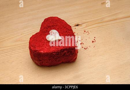 Romantic Dessert on Wooden Surface. Heart-shaped cake with a small white chocolate heart decoration is presented. Valentine's Day concept phtp. Stock Photo