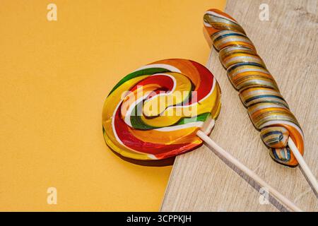 Two colorful lollipops resting on a wooden surface against a bright orange background. This cheerful image is perfect for projects related to fun. Stock Photo