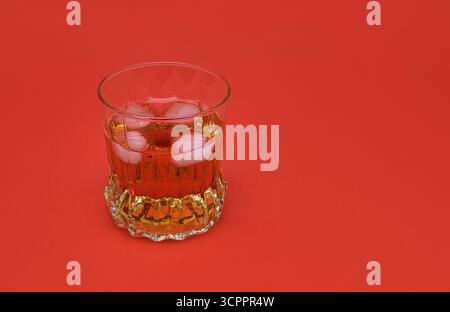 Isolated crystal glass filled with whiskey and ice cubes on red background. Object for themes related to luxury, nightlife and celebration. Stock Photo