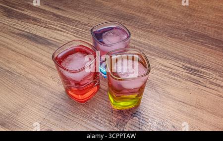 Trio of colorful cocktails. Three vibrant cocktails in square glasses with ice cubes on wooden surface. Use for nightlife and social gatherings. Stock Photo